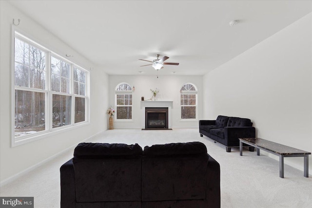 carpeted living area featuring a fireplace with flush hearth, baseboards, and ceiling fan