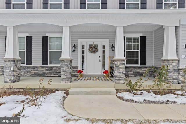 snow covered property entrance featuring stone siding and a porch