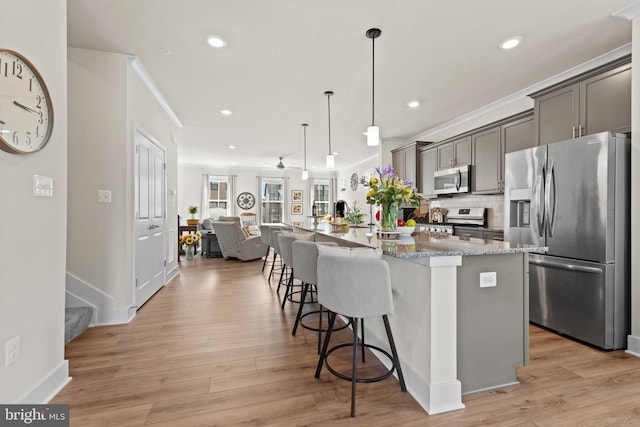 kitchen featuring a kitchen breakfast bar, open floor plan, appliances with stainless steel finishes, light stone counters, and ornamental molding