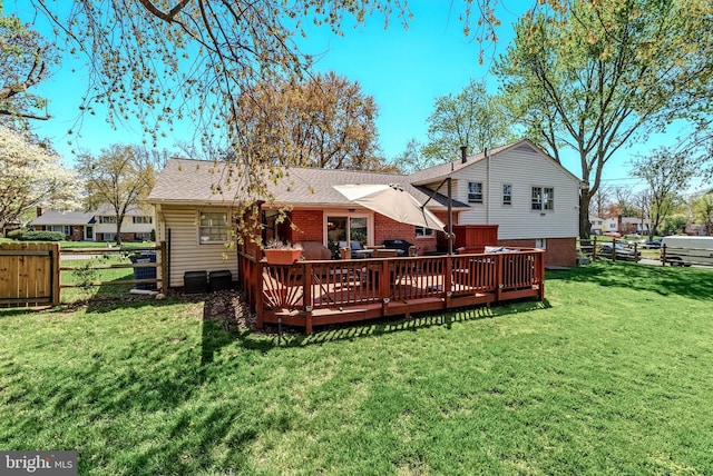 back of property with a shingled roof, brick siding, a deck, fence, and a lawn