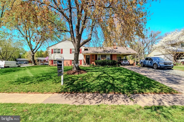 tri-level home featuring a front yard, a chimney, brick siding, an attached carport, and driveway