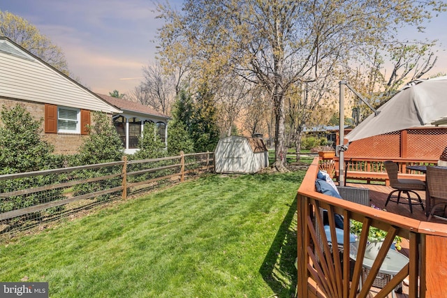 yard at dusk with a storage shed, an outbuilding, a deck, and fence