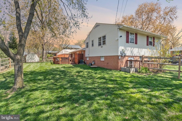 view of side of property with a deck, a shed, a yard, fence, and an outbuilding
