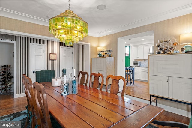 dining room with wood finished floors, a chandelier, crown molding, and wallpapered walls