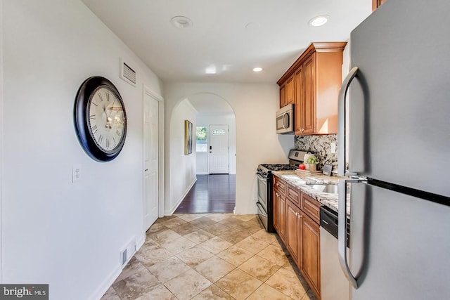 kitchen with brown cabinets, decorative backsplash, arched walkways, and stainless steel appliances