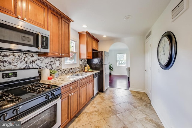 kitchen featuring arched walkways, visible vents, a sink, stainless steel appliances, and brown cabinets