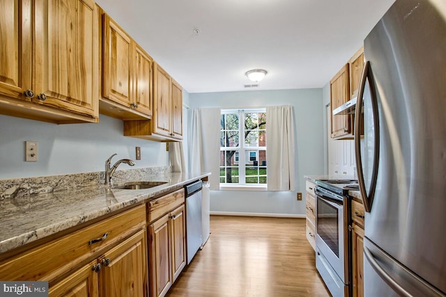 kitchen featuring light stone counters, a sink, stainless steel appliances, baseboards, and light wood-style floors