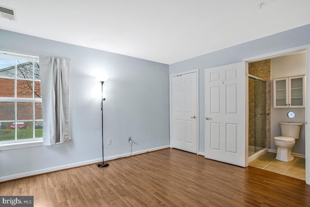 unfurnished bedroom with multiple windows, visible vents, wood finished floors, and baseboards