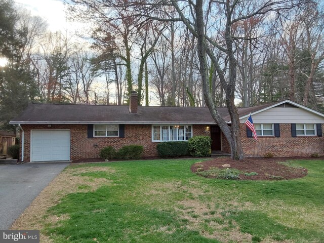 ranch-style house with a front yard, a chimney, an attached garage, and aphalt driveway