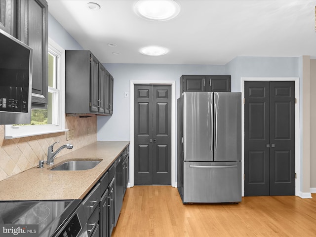 kitchen with a sink, appliances with stainless steel finishes, light wood-style floors, light stone countertops, and decorative backsplash