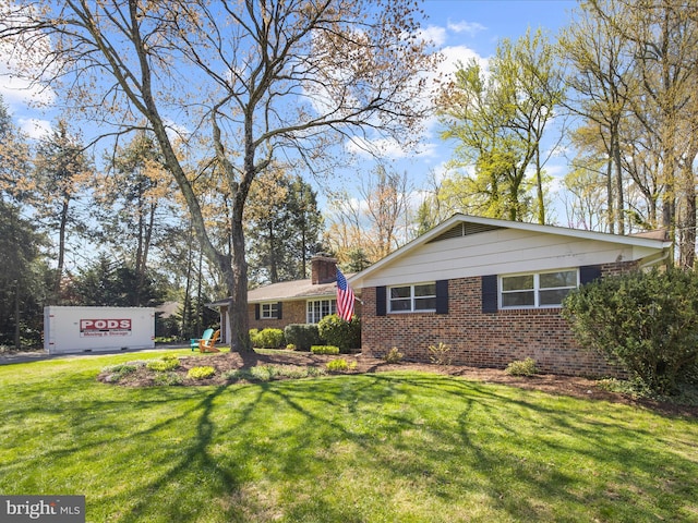 view of front facade with brick siding, a front yard, and a chimney