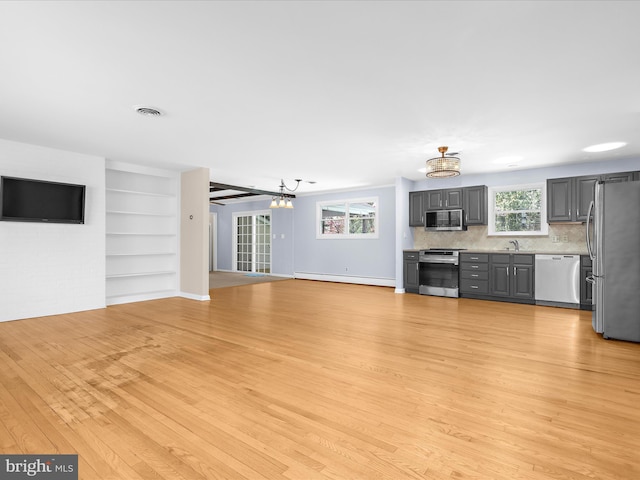 unfurnished living room with visible vents, a sink, a chandelier, light wood finished floors, and a baseboard heating unit
