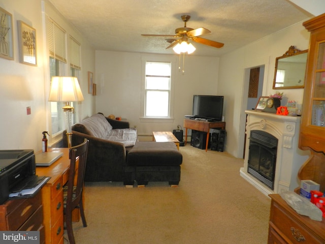 carpeted living area featuring a textured ceiling, a glass covered fireplace, and a ceiling fan