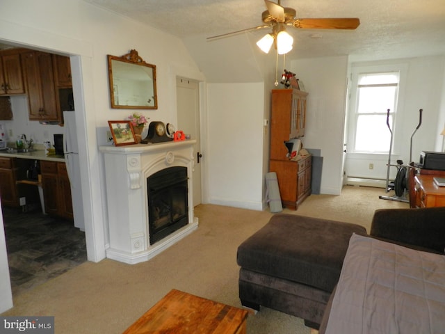 living area with ceiling fan, a glass covered fireplace, a baseboard heating unit, and light carpet