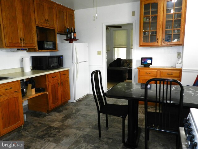 kitchen with light countertops, brown cabinets, glass insert cabinets, black microwave, and freestanding refrigerator