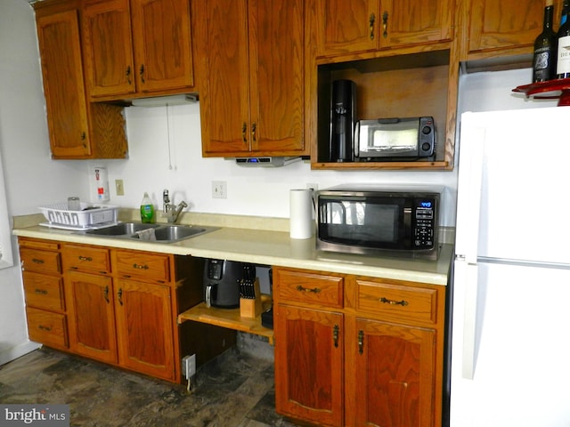 kitchen featuring freestanding refrigerator, light countertops, a sink, and brown cabinets