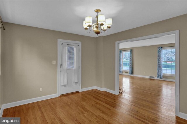 interior space with a chandelier, wood finished floors, baseboards, and visible vents