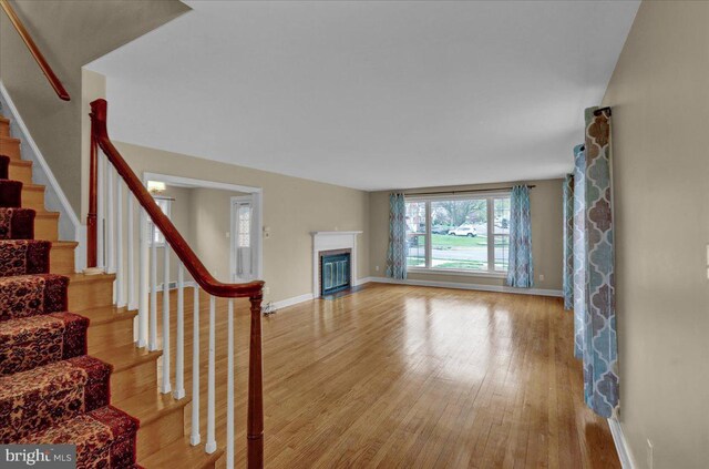 living area with wood finished floors, baseboards, a glass covered fireplace, and stairs