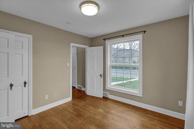 unfurnished bedroom with wood finished floors, baseboards, and visible vents