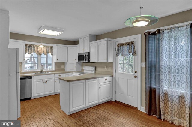 kitchen with a peninsula, light wood-style flooring, white cabinetry, appliances with stainless steel finishes, and a sink