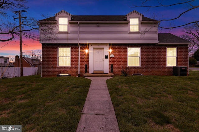 colonial inspired home featuring fence, a front yard, central AC unit, and brick siding