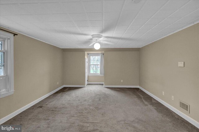 carpeted empty room with baseboards, a ceiling fan, and visible vents