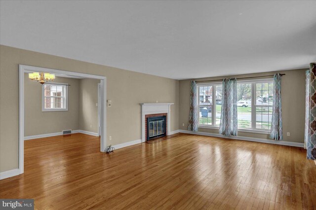 unfurnished living room featuring a fireplace, plenty of natural light, an inviting chandelier, and wood finished floors