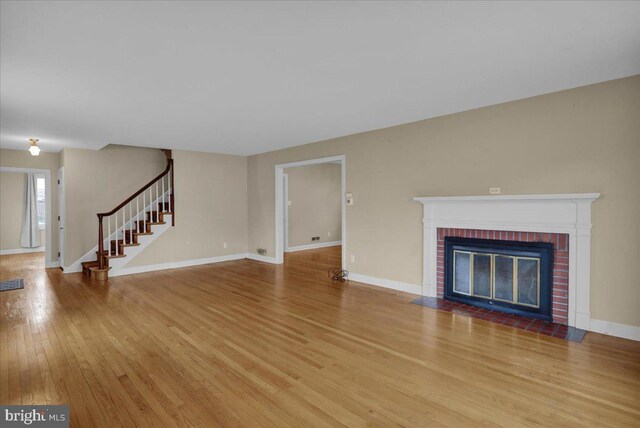 unfurnished living room with a fireplace, baseboards, stairs, and wood finished floors