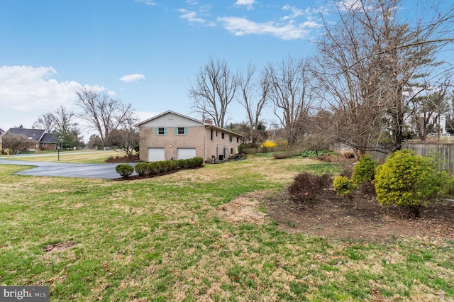 view of yard featuring asphalt driveway and a garage