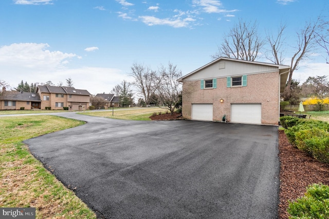 view of property exterior with a garage, asphalt driveway, brick siding, a yard, and a residential view