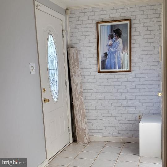entrance foyer with light tile patterned flooring and brick wall