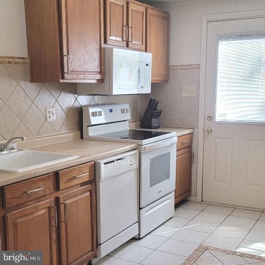 kitchen with a sink, brown cabinetry, light countertops, and white appliances
