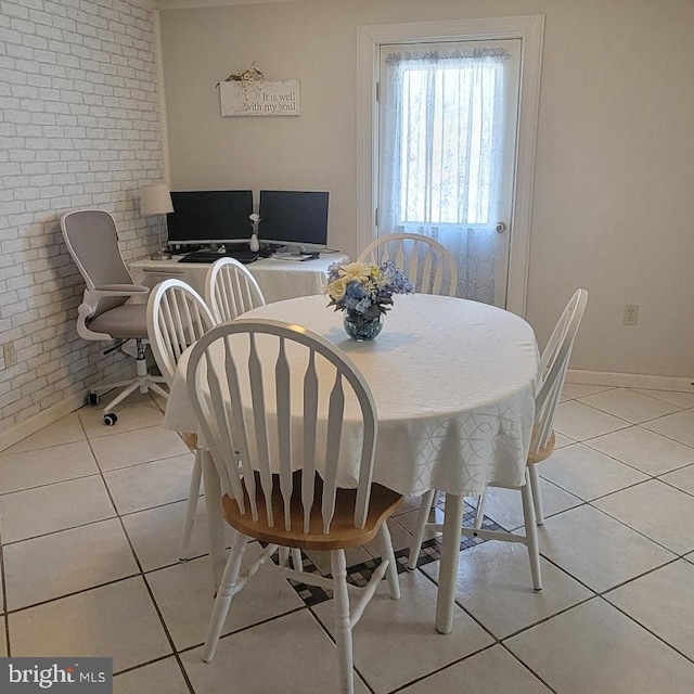 dining room featuring brick wall, light tile patterned flooring, and baseboards