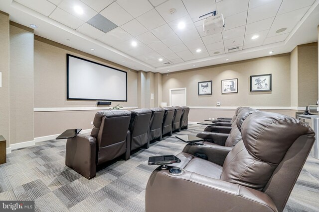home theater room with light colored carpet, a raised ceiling, visible vents, and baseboards
