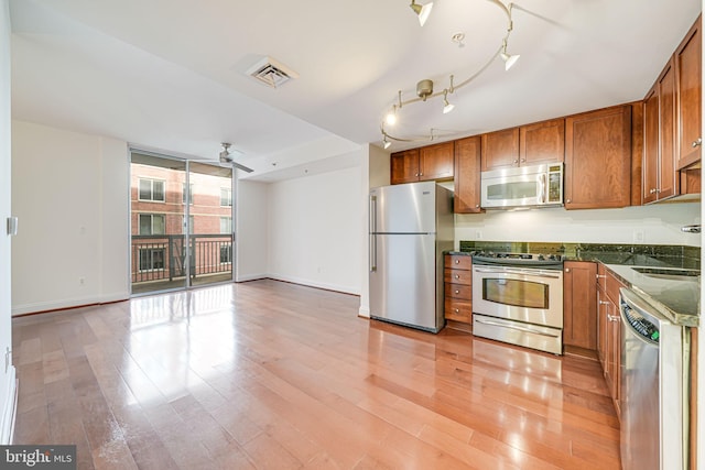 kitchen with brown cabinets, light wood-style flooring, stainless steel appliances, and baseboards