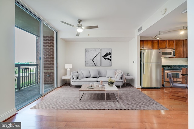 living room featuring expansive windows, visible vents, light wood finished floors, rail lighting, and a ceiling fan