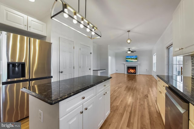 kitchen with ceiling fan, appliances with stainless steel finishes, light wood-style floors, white cabinetry, and a lit fireplace