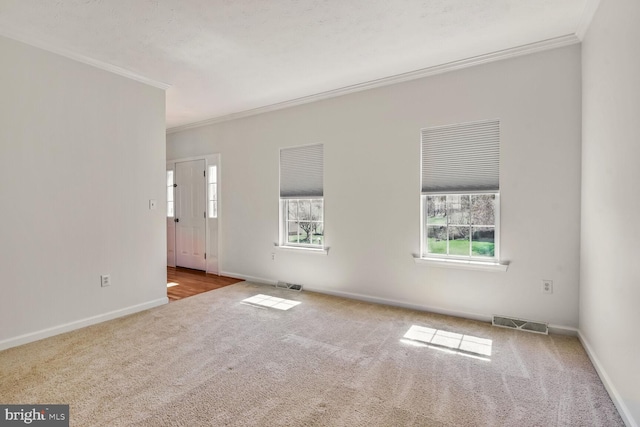 unfurnished room with carpet flooring, baseboards, ornamental molding, and visible vents