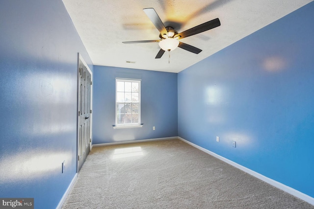 empty room featuring a textured ceiling, ceiling fan, baseboards, and carpet