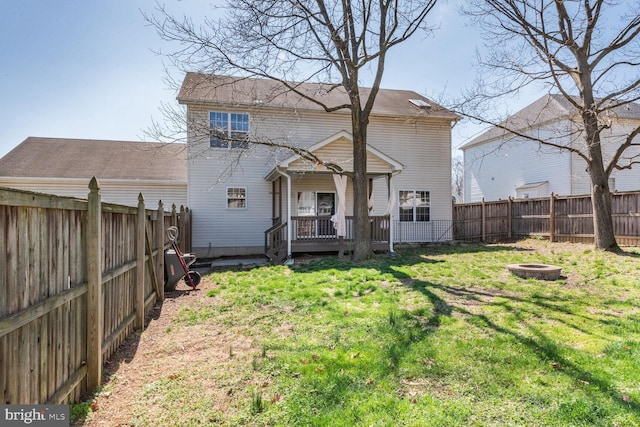 rear view of house with a fire pit, a deck, a fenced backyard, and a lawn