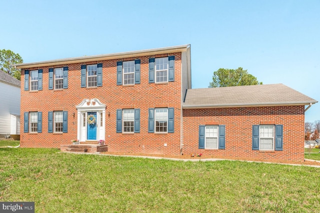colonial inspired home with a shingled roof, brick siding, and a front lawn