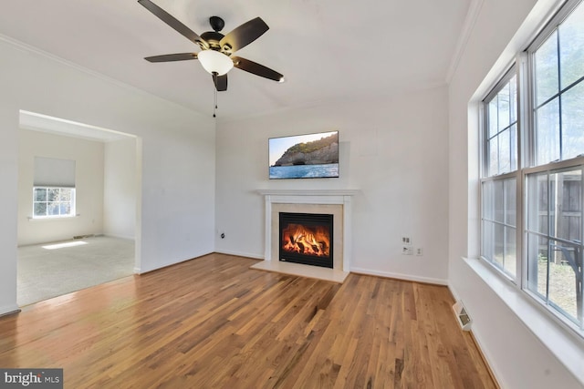 unfurnished living room with a glass covered fireplace, ceiling fan, ornamental molding, and wood finished floors