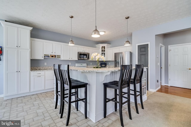 kitchen with white cabinets, light stone countertops, a kitchen bar, appliances with stainless steel finishes, and hanging light fixtures