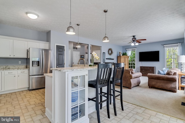 kitchen featuring ceiling fan, white cabinetry, stainless steel refrigerator with ice dispenser, light stone counters, and open floor plan