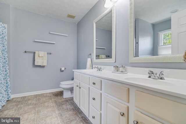 bathroom with toilet, double vanity, a sink, and baseboards