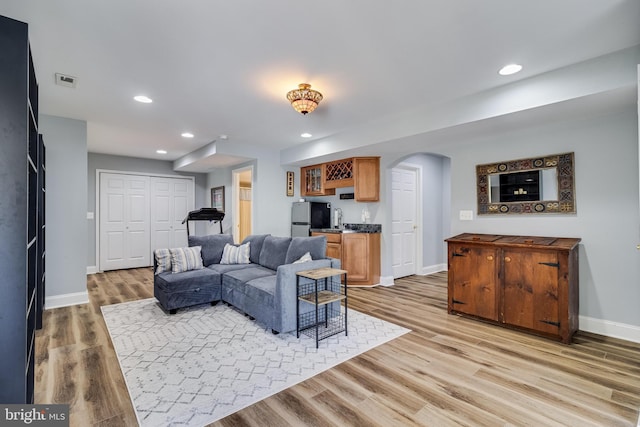 living area featuring indoor wet bar, arched walkways, light wood-type flooring, recessed lighting, and baseboards