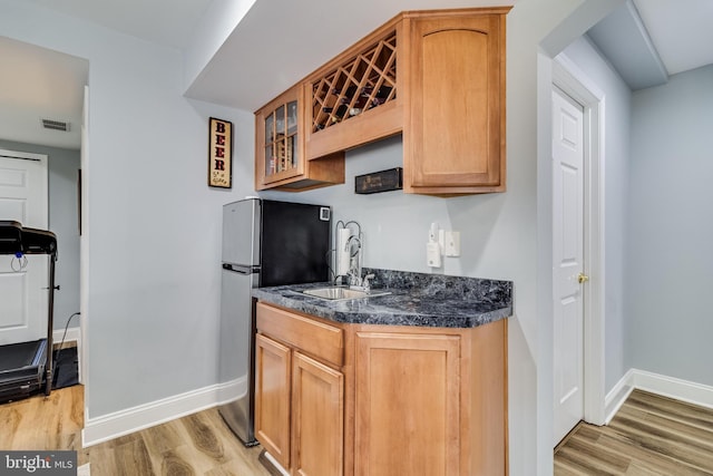 kitchen featuring light wood-style flooring, freestanding refrigerator, a sink, and glass insert cabinets