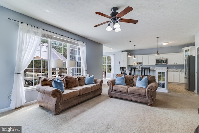 living room with baseboards, a ceiling fan, light carpet, and a textured ceiling
