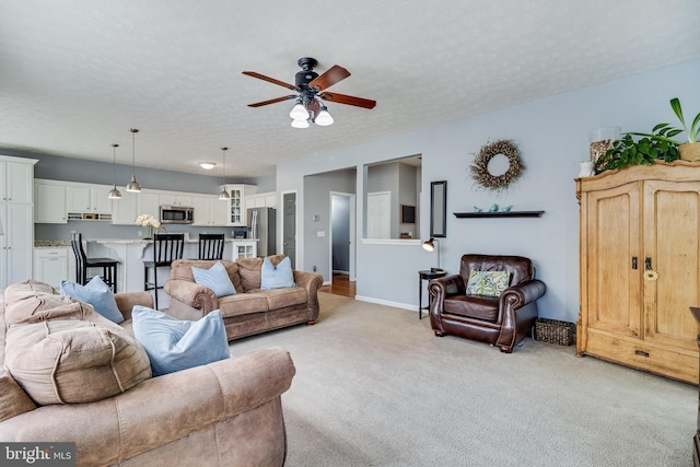living room featuring light colored carpet, ceiling fan, baseboards, and a textured ceiling