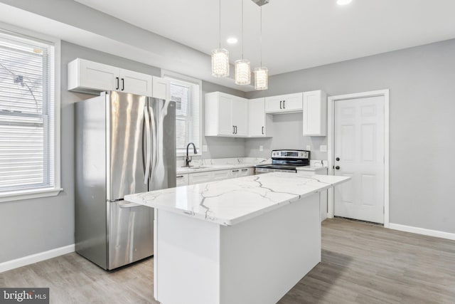kitchen featuring light wood-type flooring, white cabinetry, appliances with stainless steel finishes, light stone counters, and a sink